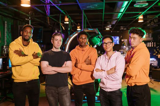 A confident and diverse group of friends standing in an arcade gaming environment.