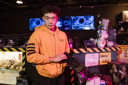 Man in Orange Zip Up Hoodie Holding a Mechanical Keyboard