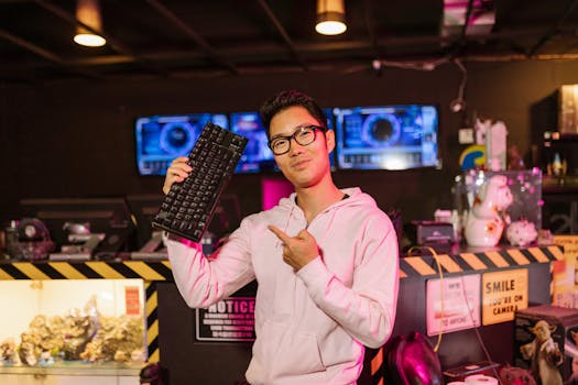 Man in a gaming setup holding and pointing at a mechanical keyboard, exuding enthusiasm.