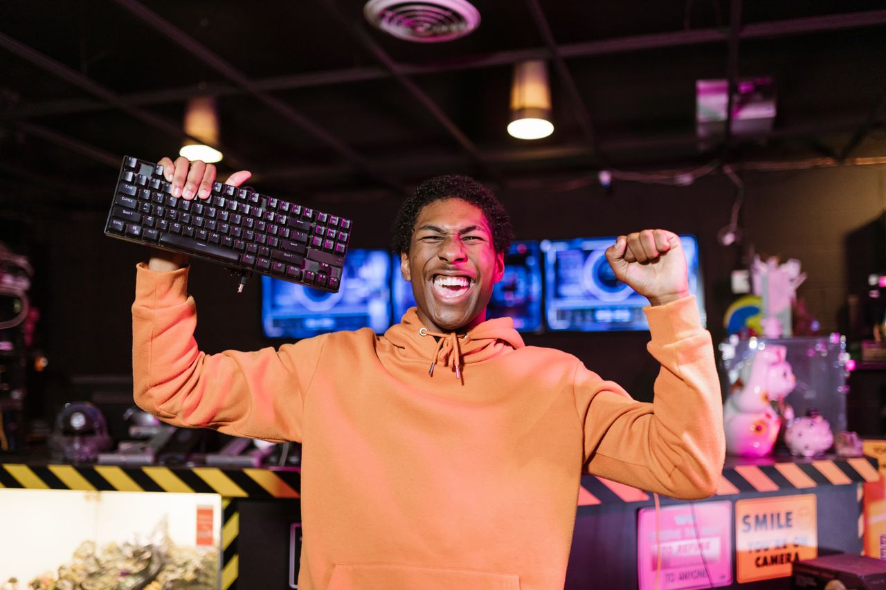 joyful man in orange jacket celebrating gaming victory with a keyboard