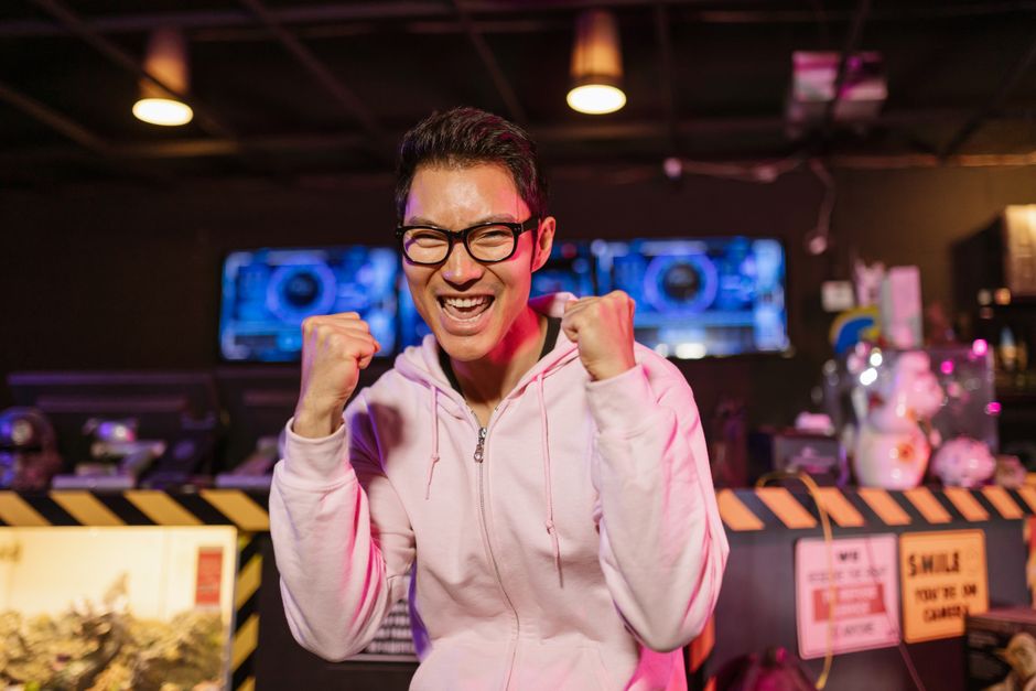 フーディを着た興奮したゲーマーが、屋内で喜びの笑顔を浮かべて勝利を祝う。