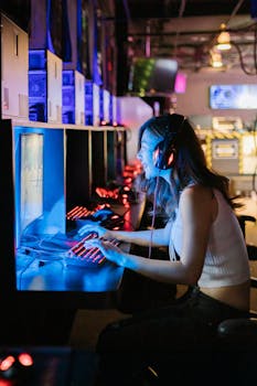 A woman intensely focused on a gaming computer in an esports setting with vibrant lighting.
