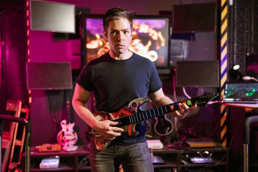 Man playing a guitar controller in a vibrant gaming room. Perfect for e-sports and recreation themes.