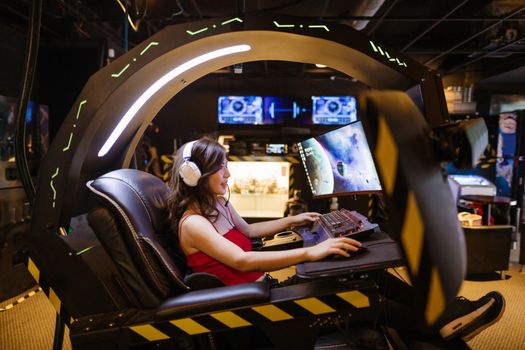 A woman plays a video game in a high-tech scorpion gaming chair, immersed in a modern arcade.