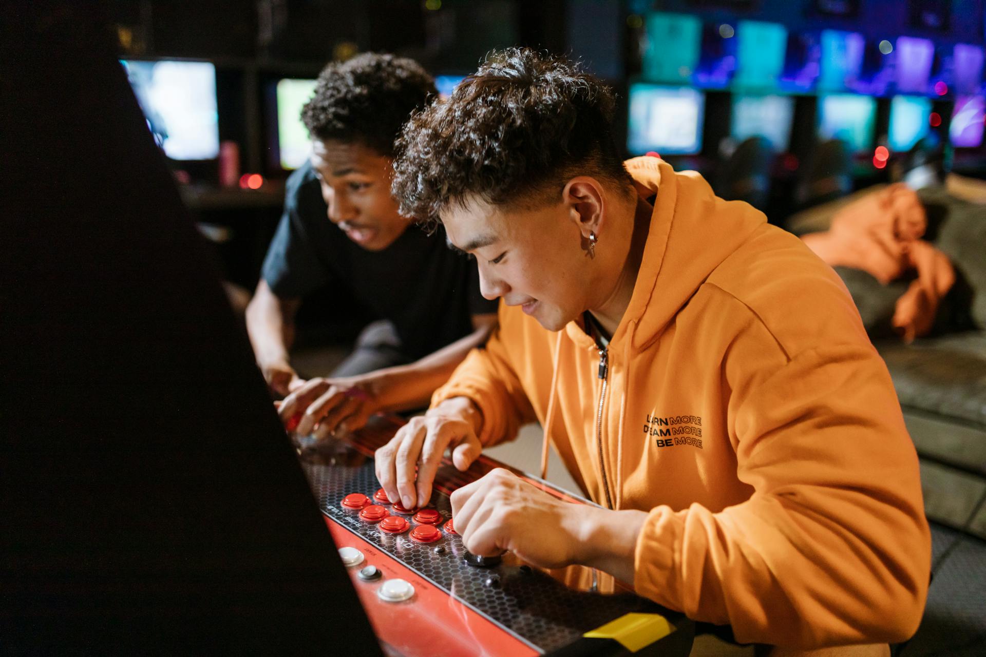 Two friends enjoying a video game session on an arcade machine indoors.