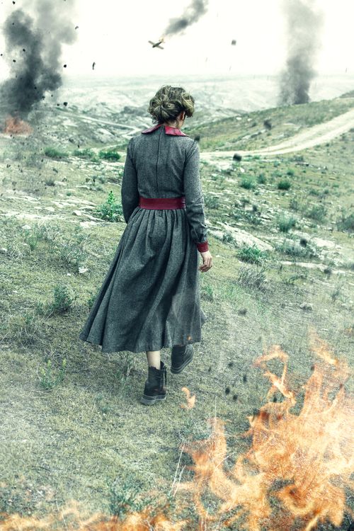 Free Woman in historical dress walks on a smoky battlefield with fires and explosions around. Stock Photo