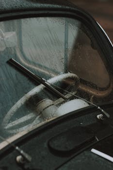 Detailed view of a vintage car's steering wheel and windshield on a rainy day.