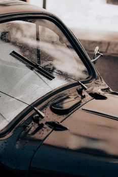 Close-up of a vintage car with raindrops on windshield, showcasing classic design and rainy atmosphere.