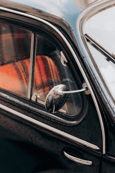 Detailed view of a vintage car's side mirror and window with raindrops.