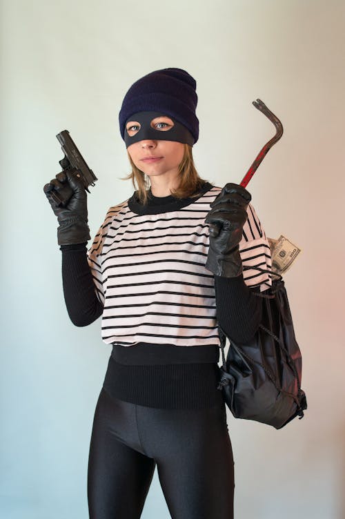 Free A Person Wearing Mask Holding a Gun and a Hand Tool Carrying a Bag of Money Stock Photo