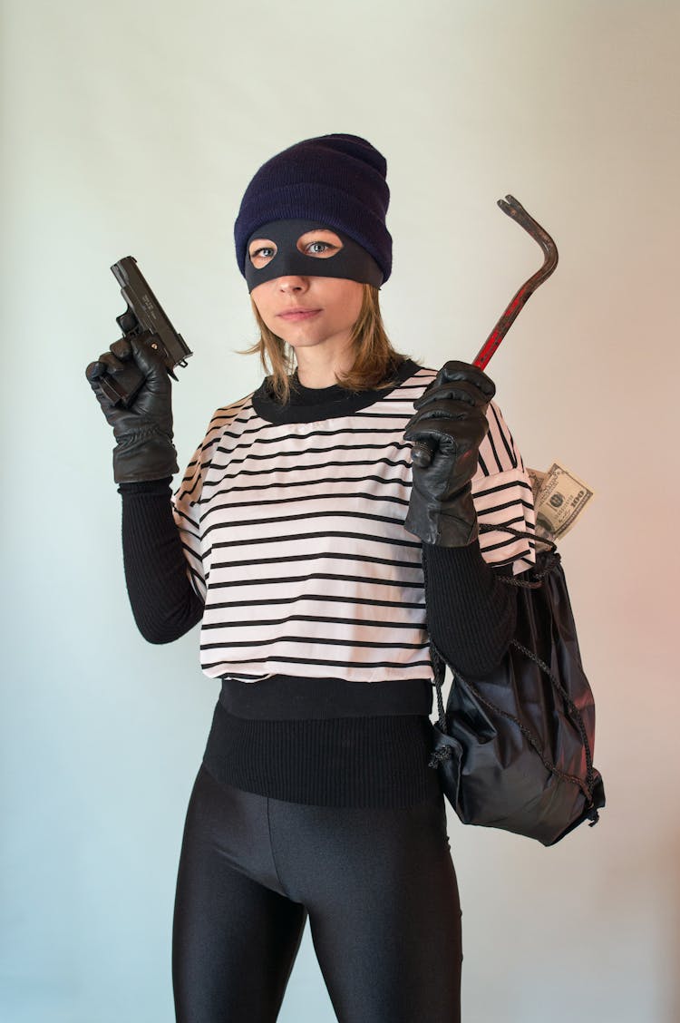 A Person Wearing Mask Holding A Gun And A Hand Tool Carrying A Bag Of Money