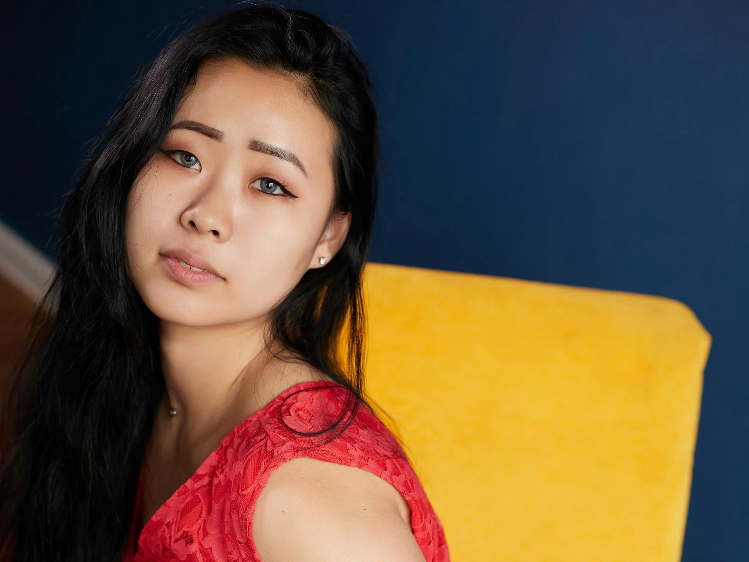 A beautiful woman in a red dress sitting indoors with a contemplative expression.