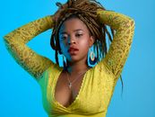 Portrait of a woman with braided hair in a yellow lace top against a blue background.