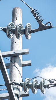 Close-up of power lines and insulators on an electric pole with blue sky background.