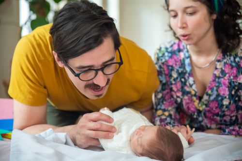 Free A tender moment captured as a happy couple gazes lovingly at their newborn baby indoors. Stock Photo