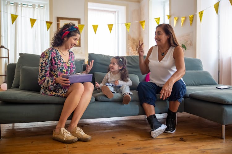 A Woman In Floral Dress Talking To The Baby Sitting Near The Woman In White Tank Top