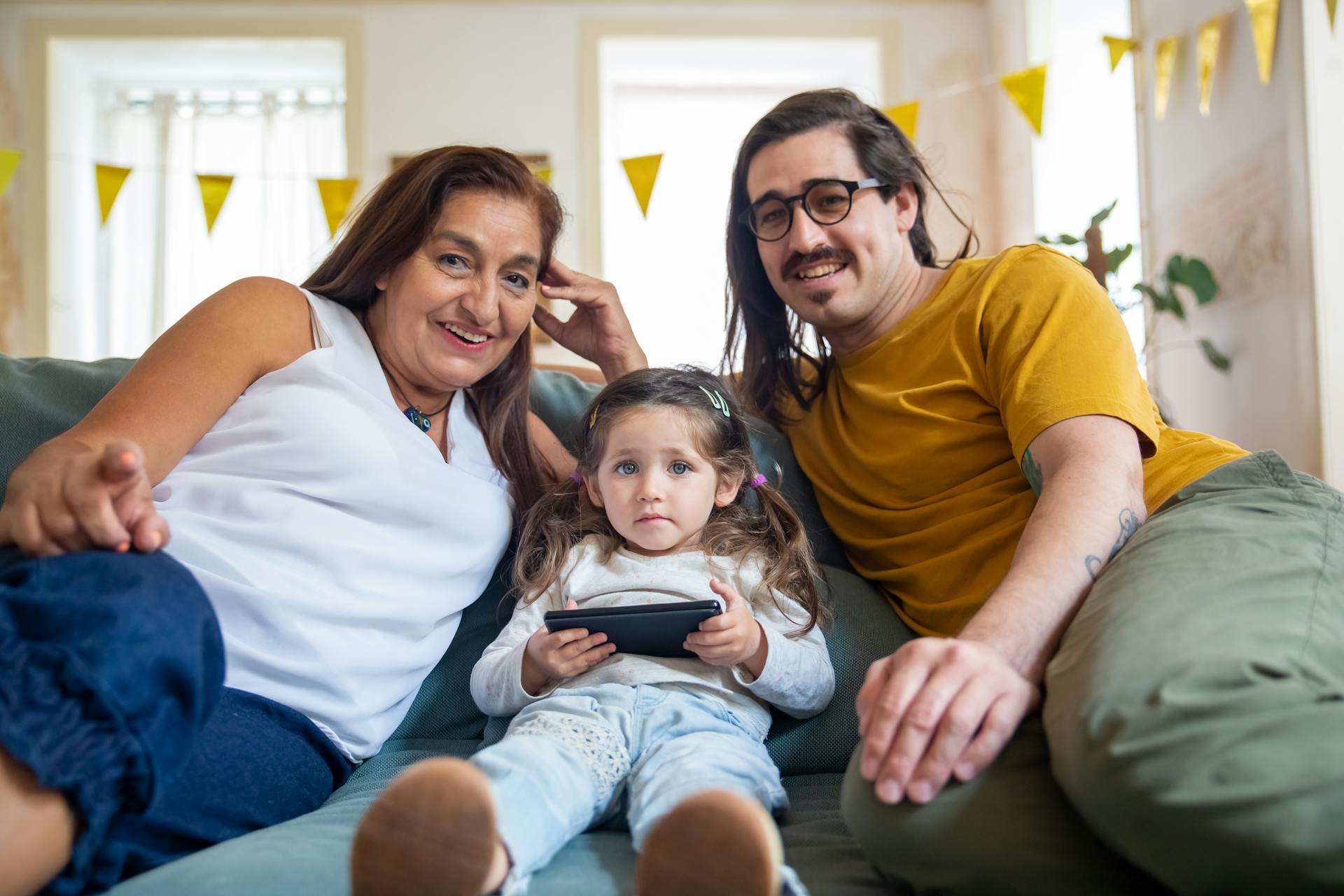 Smiling family spending quality time together indoors, with a child holding a tablet. Warm and cozy atmosphere.