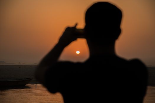 Silhouette of person photographing a beautiful sunset over the Ganges River in Varanasi, India.