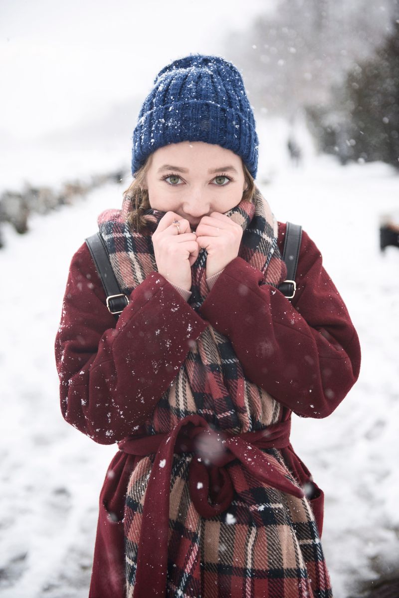 Young woman in plaid scarf and blue knit hat in snowy park