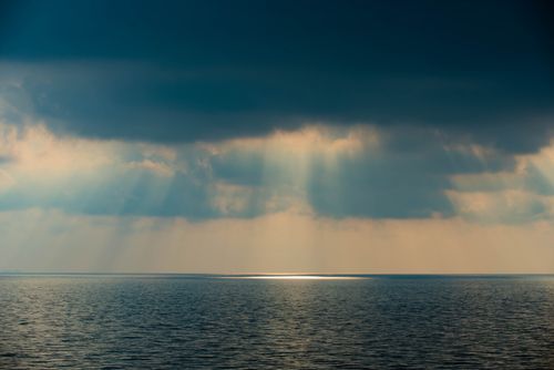 Free A serene ocean view in Singapore with dramatic clouds and sunbeams illuminating the sea. Stock Photo