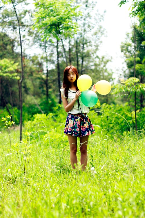 Woman Standing on Grass Field While Holding Three Balloons