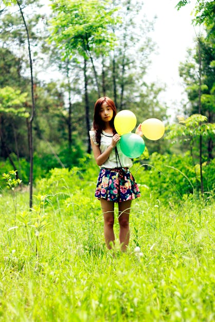 Woman Standing on Grass Field While Holding Three Balloons · Free Stock ...