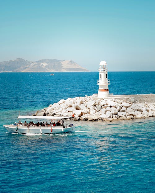 People on a Boat Near a Lighthouse on Body of Water