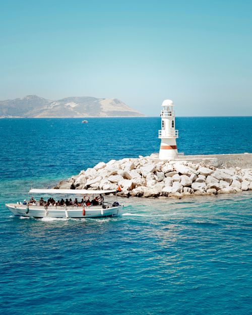 Free A picturesque lighthouse with a nearby tourist boat cruising on a sunny day. Stock Photo