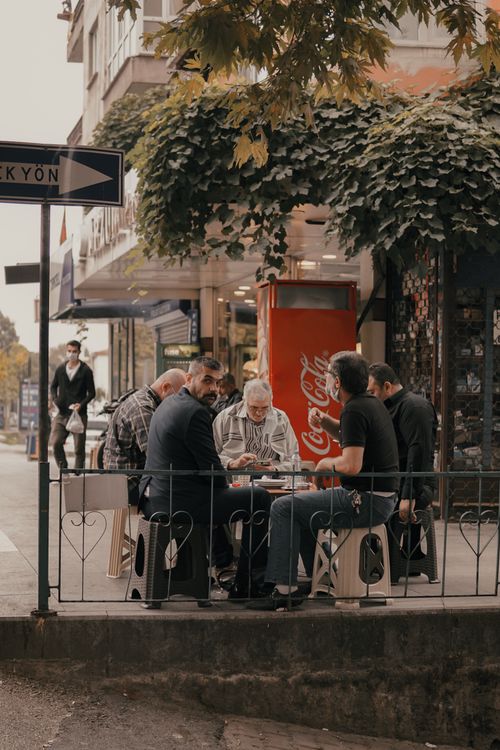 Free A group of men socializing outdoors at a cafe in İzmit, Türkiye, with a Coca-Cola vending machine nearby. Stock Photo