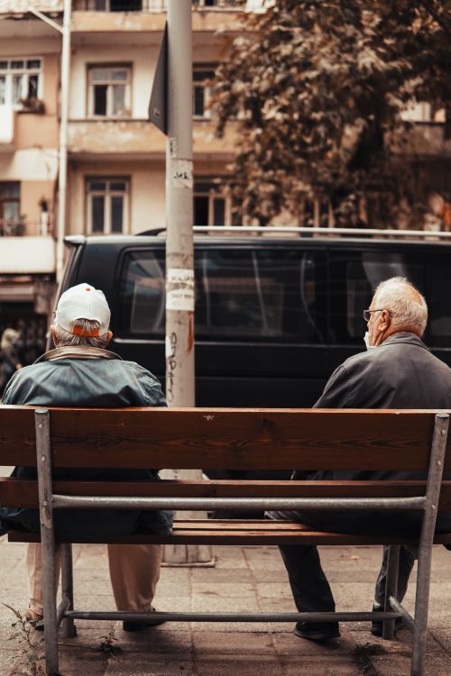 Free Two senior men sit on a bench in a busy street in İzmit, Kocaeli, capturing a candid urban scene. Stock Photo