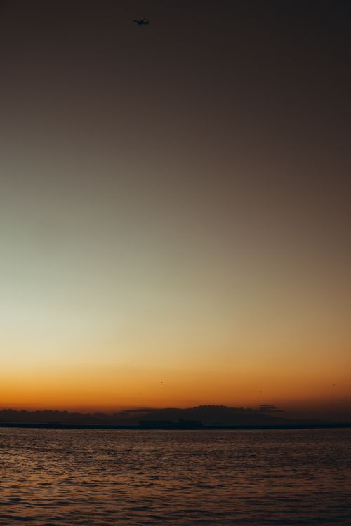 Free A serene sunset over the İzmir sea with an airplane silhouette, captured in warm tones. Stock Photo