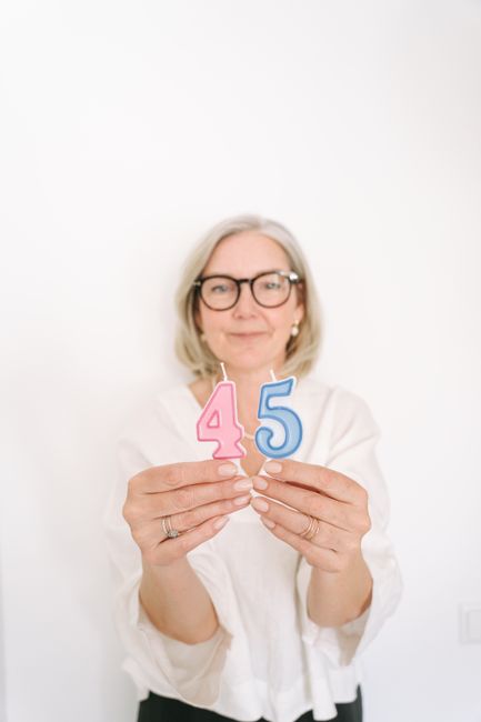 A senior woman holding number candles for a 45th birthday celebration.