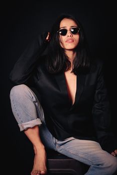 Fashion portrait of a woman in a black blazer and sunglasses posing confidently in a studio setting.