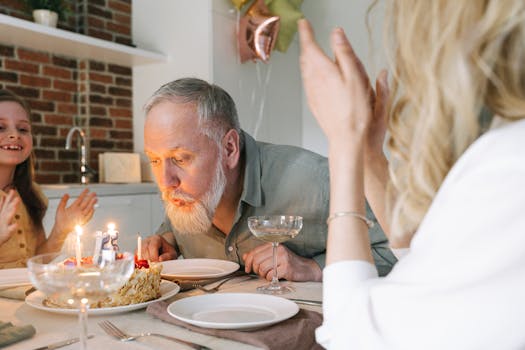A senior man celebrates his birthday by blowing out candles on a cake in a cozy indoor setting.
