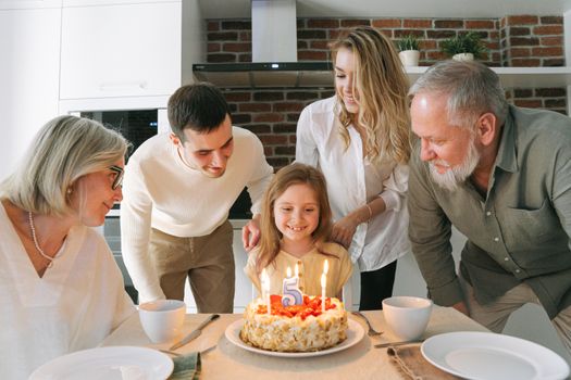 A joyful family gathered around a birthday cake to celebrate a young girl's fifth birthday.