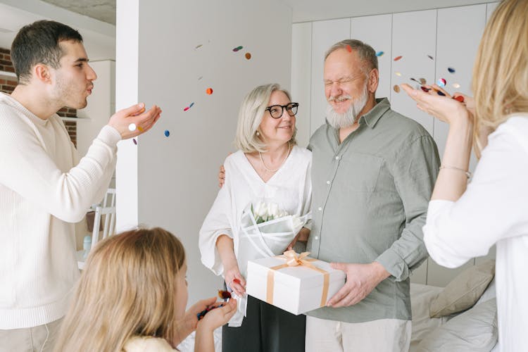 A Man And A Woman Blowing Confetti To An Elderly Couple