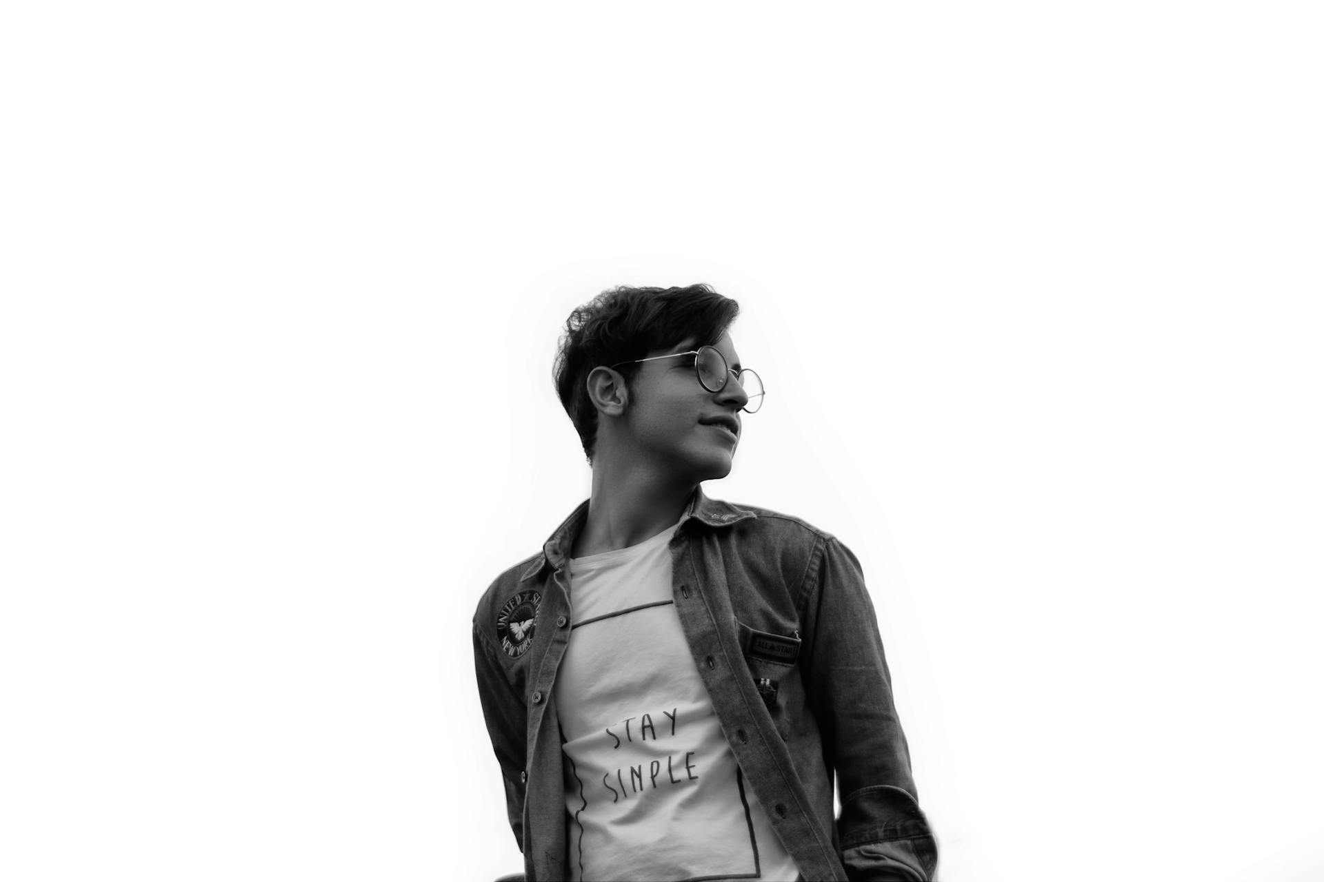 Artistic black and white photo of a young man wearing stylish eyewear and a casual outfit.