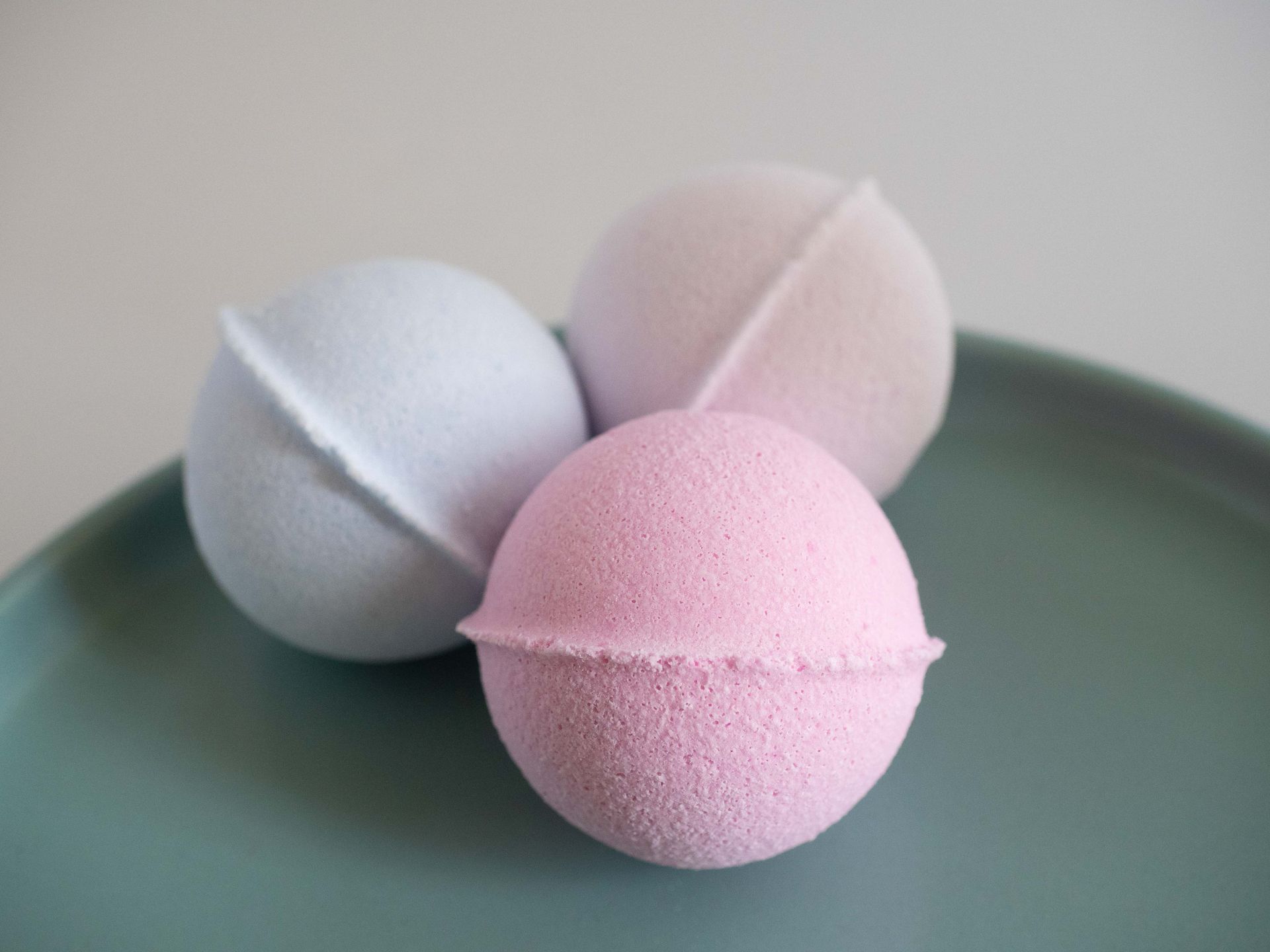 Three vibrant bath bombs displayed on a green ceramic plate, perfect for a spa setting.