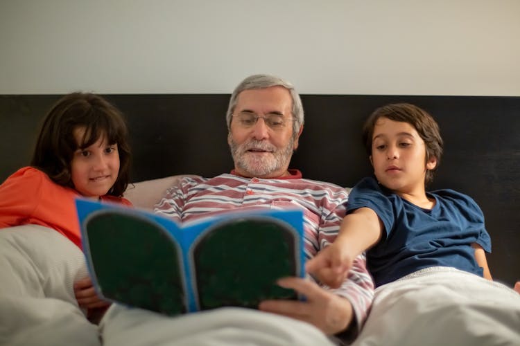 An Elderly Man Reading A Book With His Grandchildren