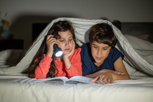 Free A Girl and a Boy Under a Blanket Reading a Book Stock Photo