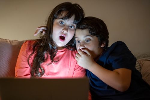 Free Two siblings experiencing a shocking moment while watching a tablet together at night. Stock Photo