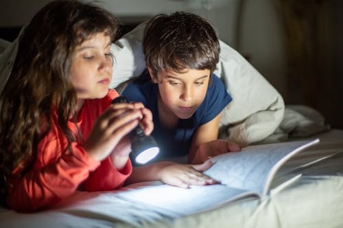 A Girl Holding a Flashlight and a Boy Reading a Book