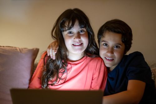 Free A brother and sister sit closely together using a laptop indoors, smiling warmly. Stock Photo