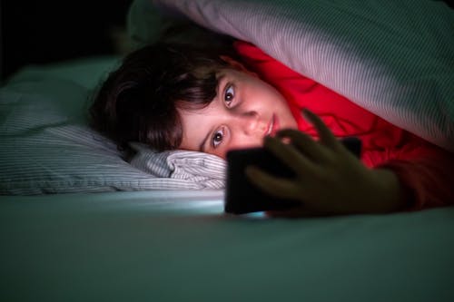 Free Boy Lying on Bed Holding Smartphone Stock Photo