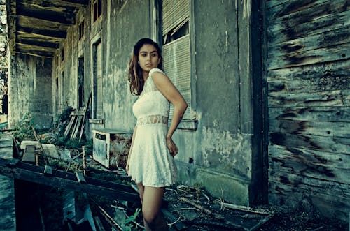 女人穿著白色禮服站在廢棄的大樓附近的照片