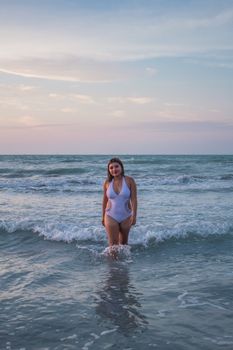 A woman in a swimsuit enjoying a serene moment in the ocean at sunset.