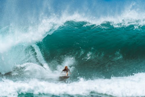 Male surfer in water suit riding surfboard on powerful blue wave while practicing extreme sport