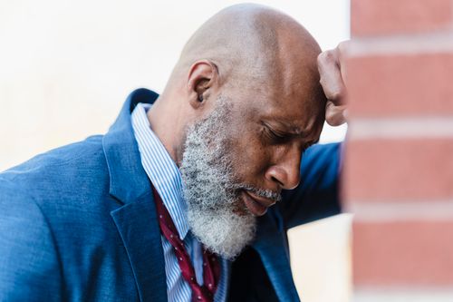 Free Side view of concerned bald African American male entrepreneur in classy suit leaning on brick wall while standing on street Stock Photo