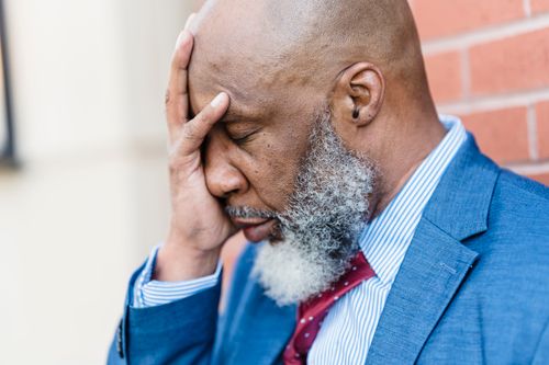 Free Side view of sad African American male entrepreneur in elegant suit covering face with hand while standing near building on street Stock Photo