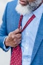 Crop unrecognizable tired male entrepreneur with gray beard adjusting red tie while standing on street in city after hard workday